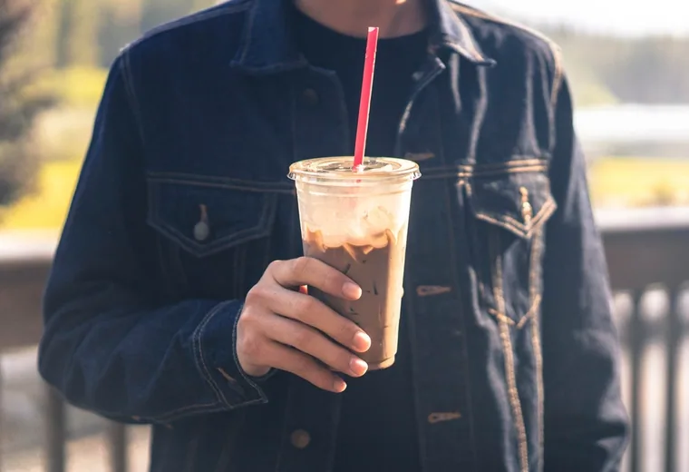 A hand holding an iced coffee with a straw